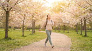 Woman walking joyfully along a sunlit path through a cherry blossom park in spring