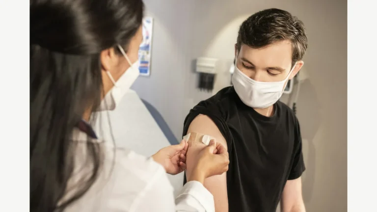 A healthcare worker places a bandage on an adult patient after vaccination.