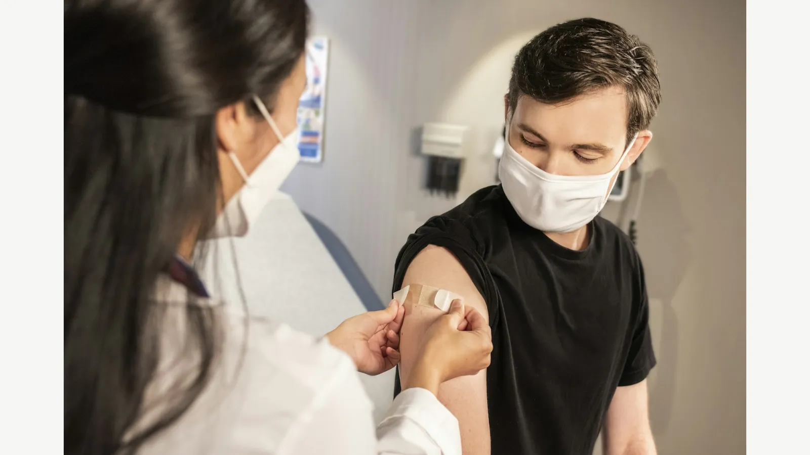 A healthcare worker places a bandage on an adult patient after vaccination.