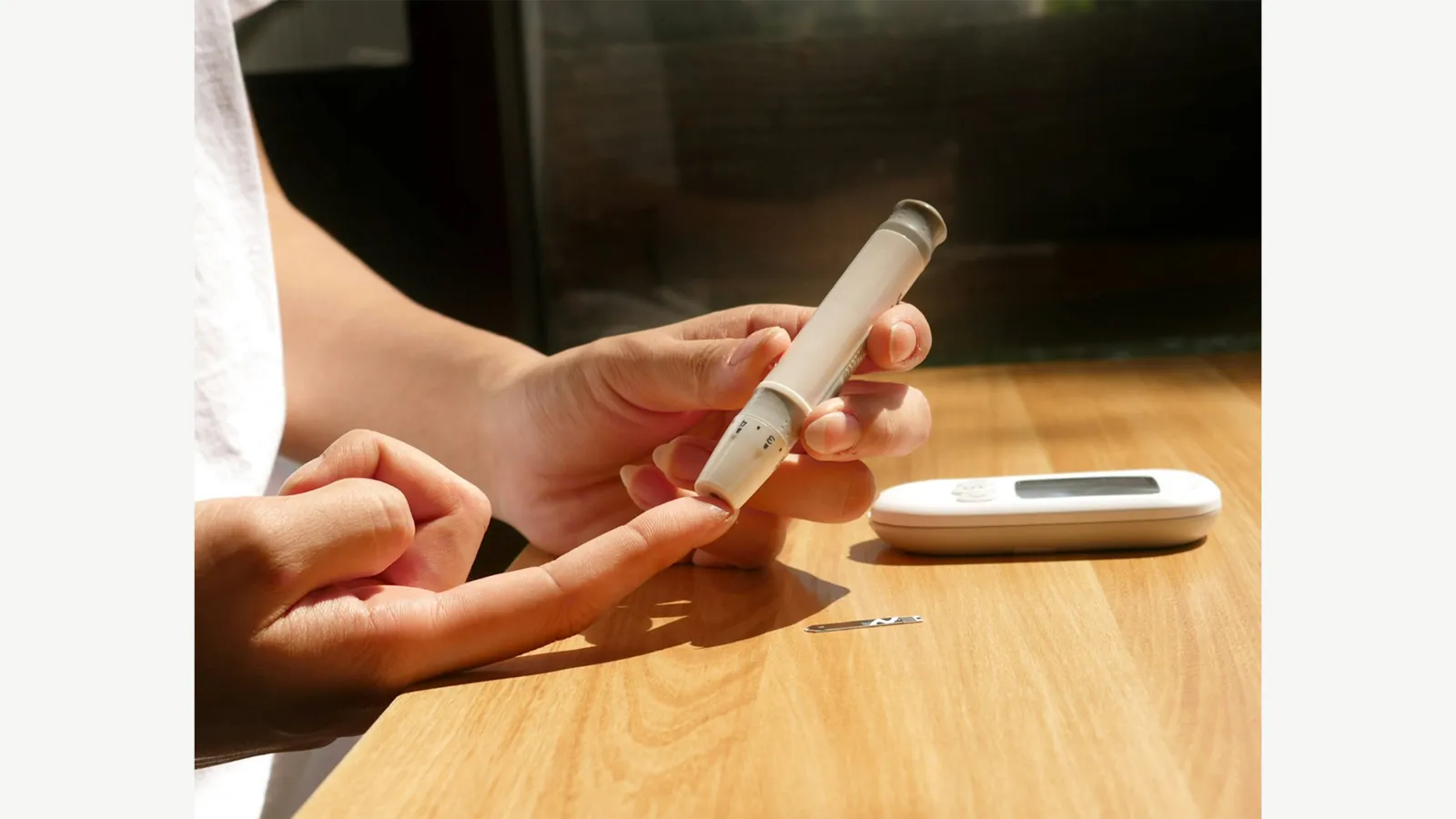 A person holding a lancing device beside a glucose meter.