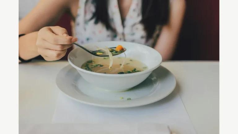 A person eating soup from a bowl at a table.