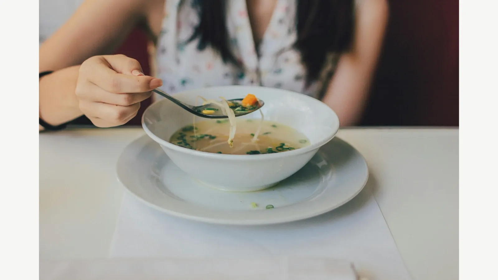A person eating soup from a bowl at a table.